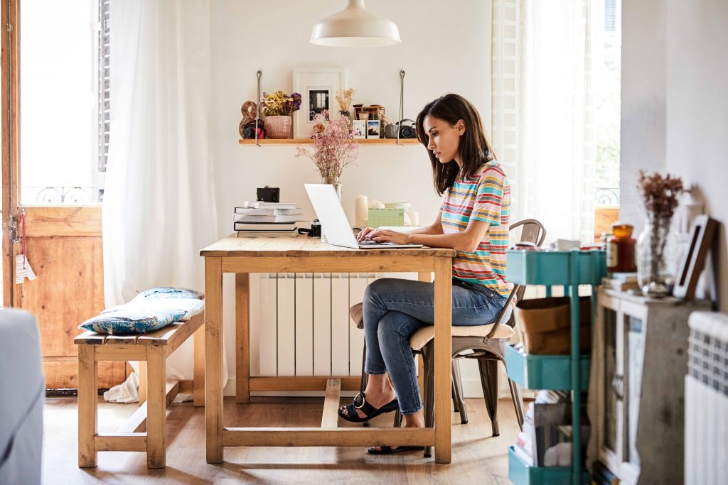 Mid adult woman using laptop at table in kitchen